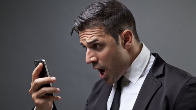 Un hombre mira con sorpresa un teléfono móvil
